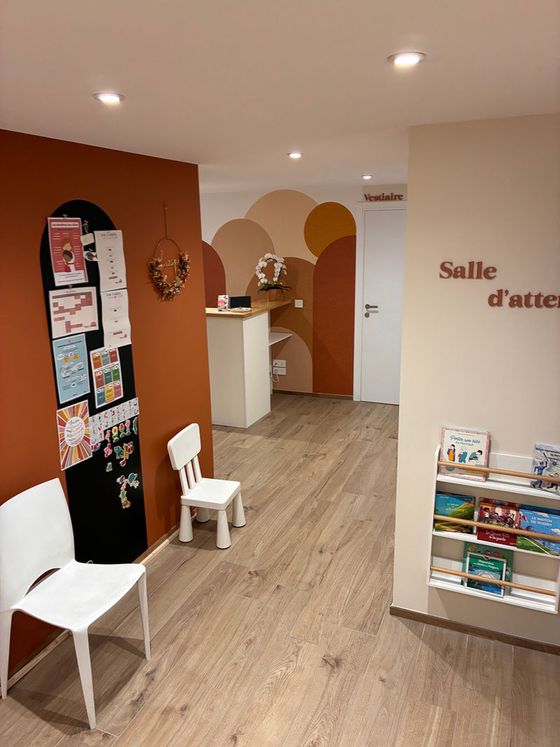 La salle d'attente avec chaises adultes et enfants et un présentoir à livres.
